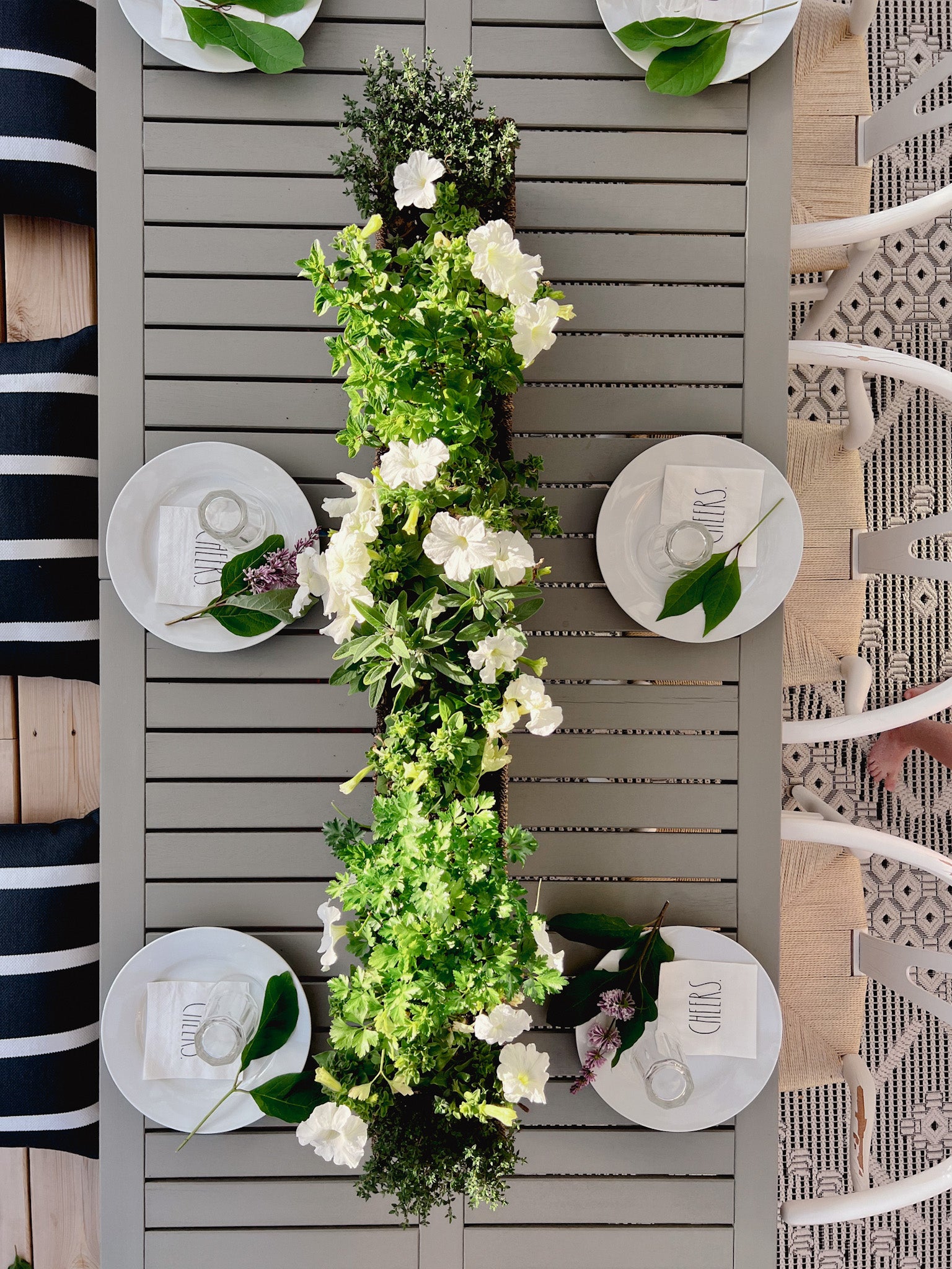 Ikea Bondholmen Dining Table with white wishbone chairs set for an outdoor dinner party with white dishes. Petunia and herb planter decorates the outdoor dining table