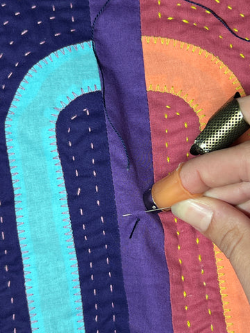 A needle is being held in a position to more easily pop a quilting knot through the quilt's fabric.