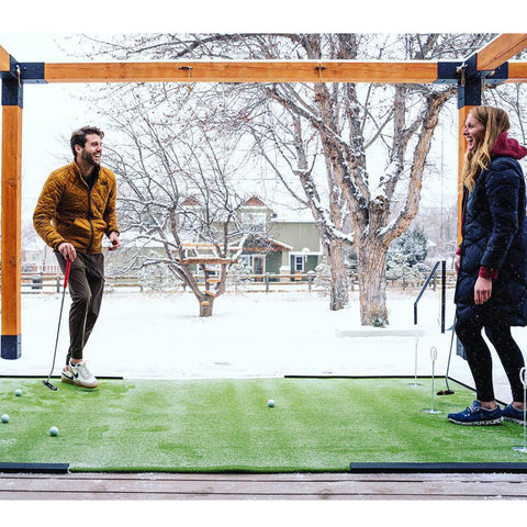 A couple playing on the putting green on an outdoor patio in the snowy winter