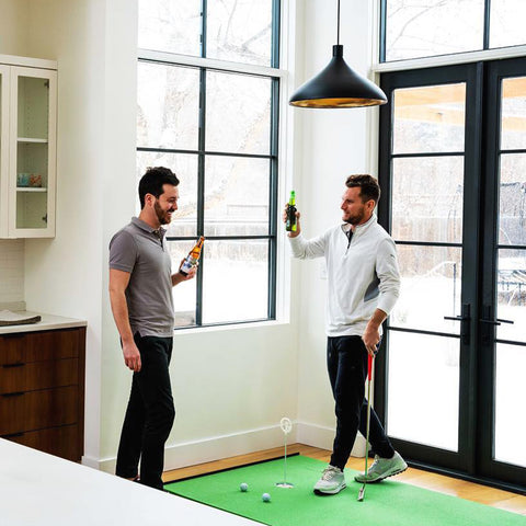 two men cheersing beers while playing on the putting green