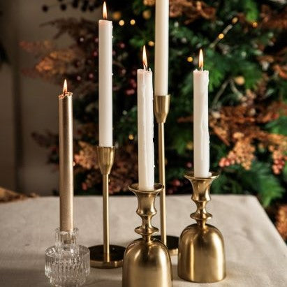 Five lit white taper candlesticks in different shaped gold candlestick holders
