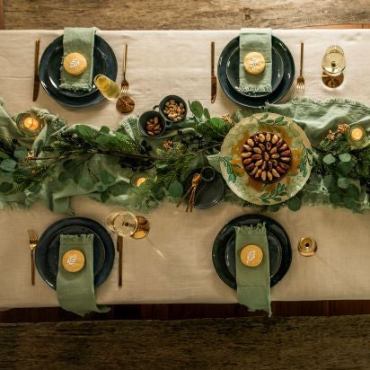 Birds-eye view of a set table with blue plates, gold cutlery and sage green table runner and napkins.