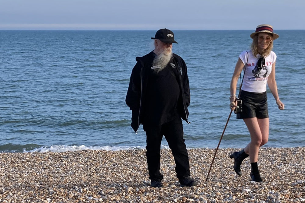 Two people—Savage Pencil and Kirsty Allison—stand on the shingle of Margate Beach
