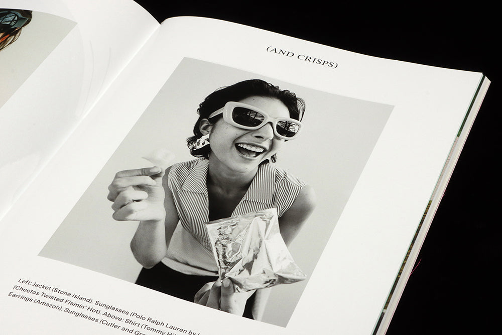 A shiot from the crisps fashion shoot: a woman in shades smiles to the camera as she holda up a crisp