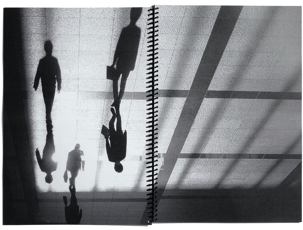 Double page spread of black and white photo of people walking with their shadows, taken from above.