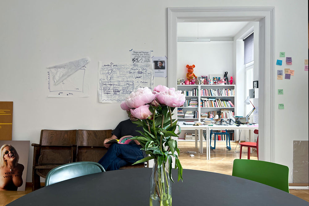 A view of the office, with vase of floweres in the foregroudn and bookshelf in the background