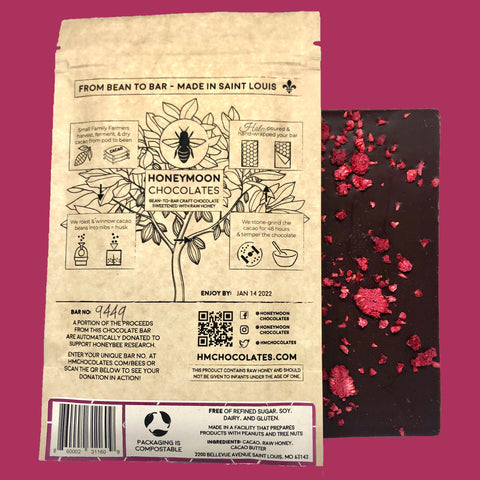 A photo of Honeymoon Chocolate's 70% Peruvian Dark Raspberry bar, the back of the bar is facing the camera so the raspberries are exposed and it is next to the packaging