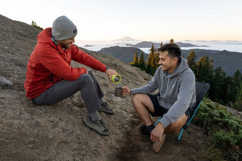 Two men enjoying hot drinks on a mountain top