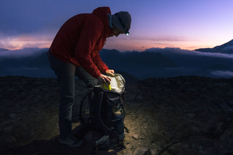 Man putting EcoSimmer into backpacking backpack on mountain at sunset