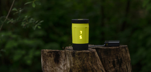 Electric camping stove plugged into battery and cooking on tree stump in nature