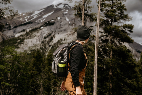 Woman looks at mountains in distance with flameless camping stove in backpack