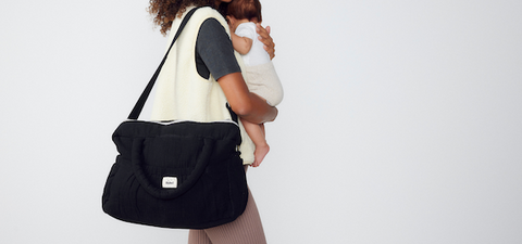 image d'une jeune maman tenant son bébé dans les bras avec un sac à langer bebel noir porté à l'épaule
