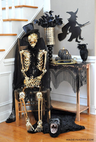 Black and gold Halloween entryway. Golden skeleton sitting in chair with top hat.