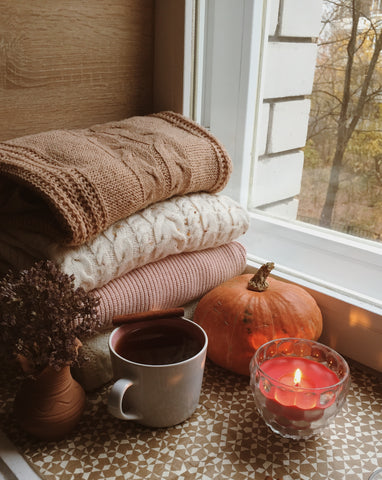 Autumn decor featuring Autumn decor featuring a cozy pile of woven blankets with orange pumpkin, cup of coffee, and candle lit.