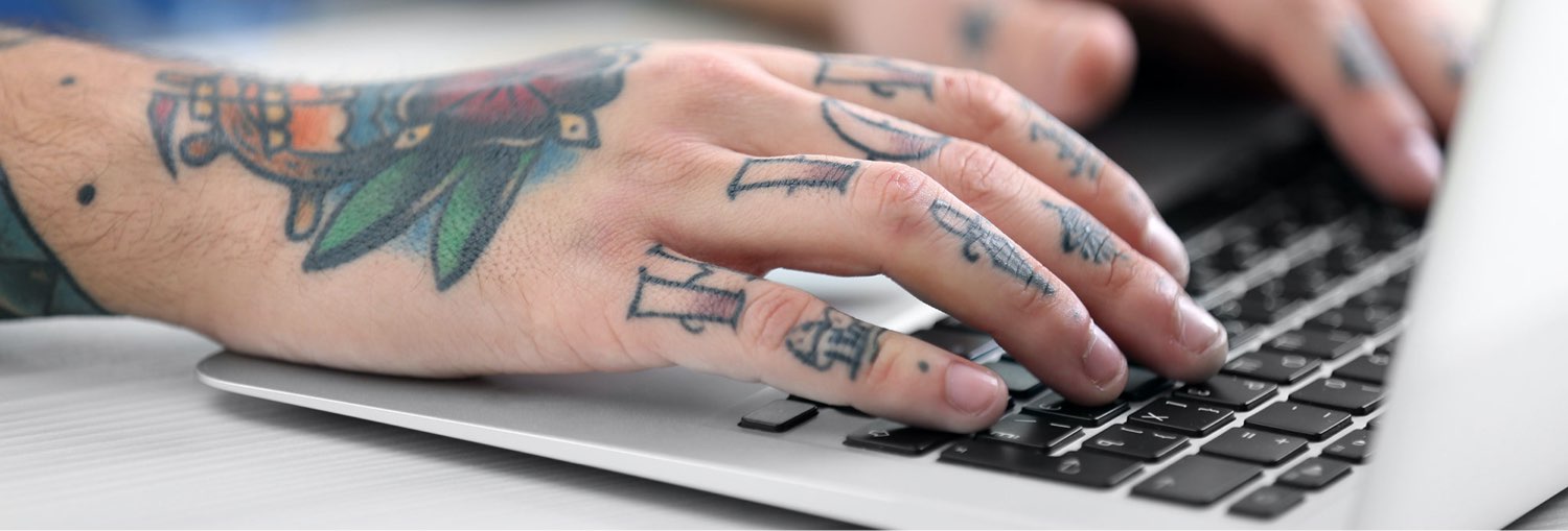 Tattooed hands typing on laptop keyboard