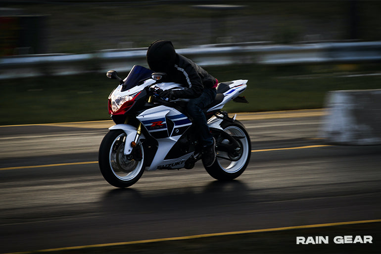 A biker, wearing Maximo Moto rain gear, rides through the rain, showcasing the effectiveness of the waterproof outfit in wet conditions.