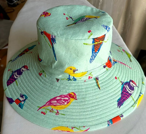 Fabric hat on an ironing board. Fabric in hat is bright birds printed on a mint colored background