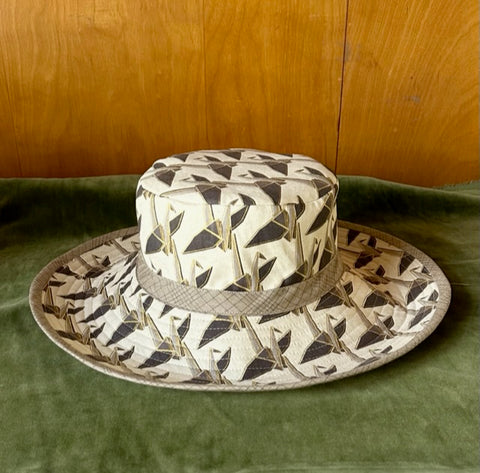 Fabric hat sitting on green velvet. Fabric of hat is printed origami cranes on an offwhite background.