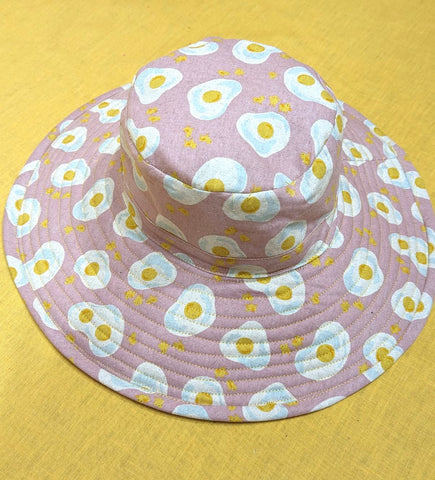 Fabric hat on a yellow surface. Hat fabric is fried eggs on a pink background.