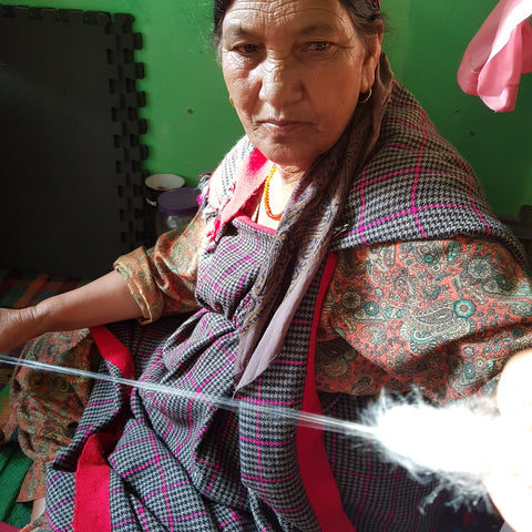 artisan woman in India gazes intently at wool she is spinning with a spindle to make yarn