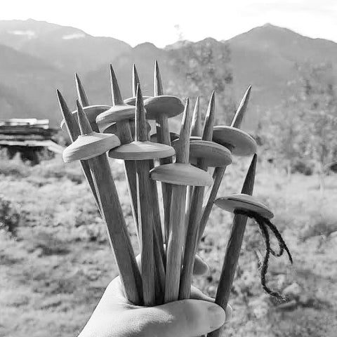 hand holds a bundle of wooden takhli spindles with mountains in background