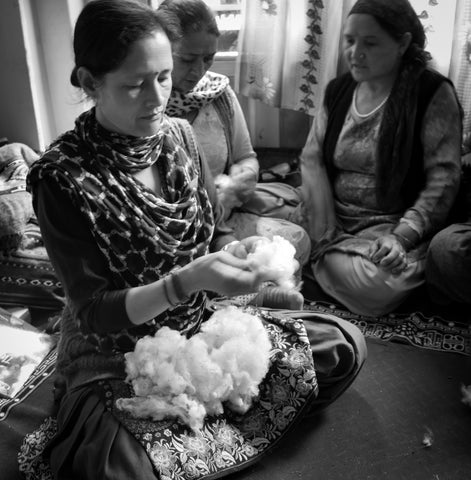 artisan woman sits on the floor picking through sheep wool