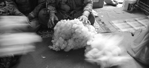 artisan woman sitting on the floor picks through a pile of sheep wool 