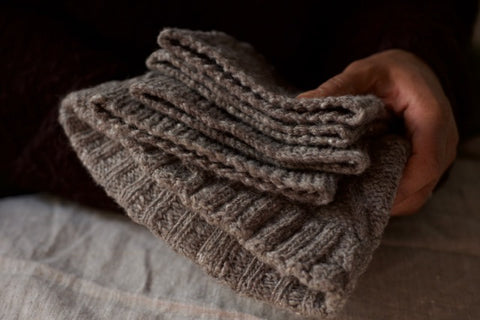 hands holding cozy dark grey wool knitted hats with dark background