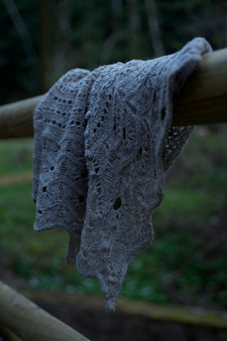 a wool handknit shawl hangs on a fence in a forest in germany