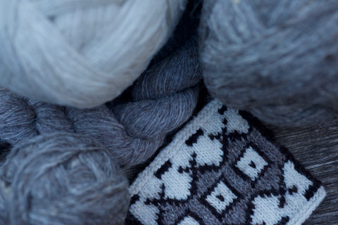 a handknit swatch pattern lies beside balls of grey and white pure wool