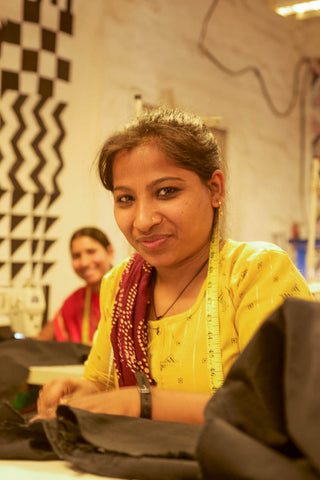 A woman sits at a sewing machine in India and looks into the camera