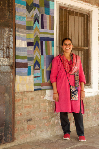 a woman in india stands in front of a quilt and rustic wall