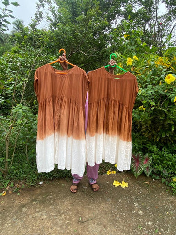 a dyer holds up two dresses that have been naturally dyed with cutch