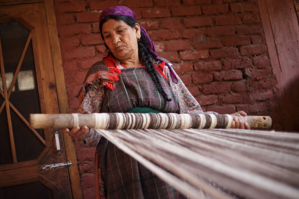elder artisan woman in India pulls on a natural wool warp for traditional handloom weaving