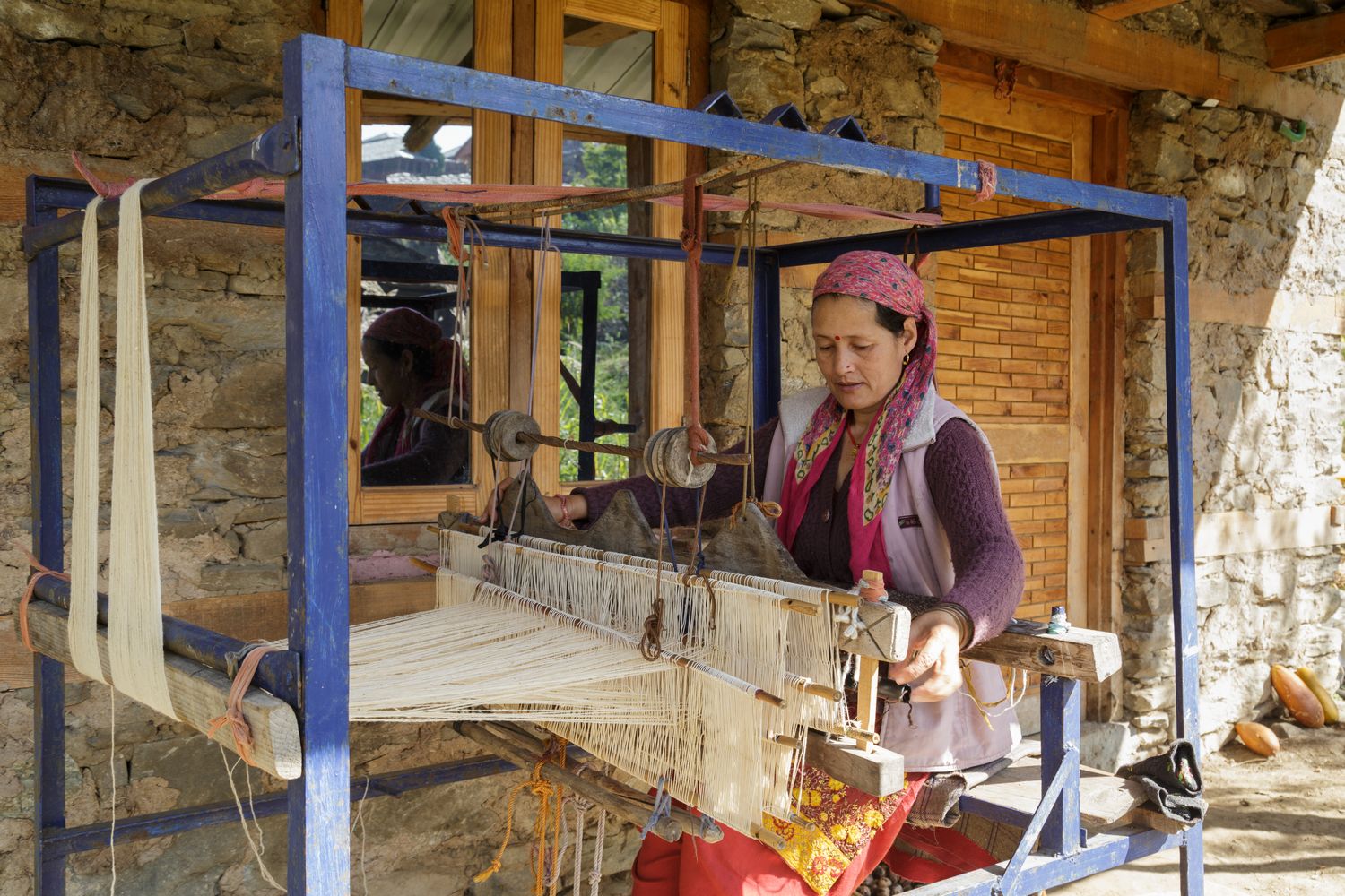 artisan woman in India sits and weaves at large traditional weaving loom in Himachal Pradesh