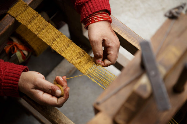  artisan woman in India weaves on a traditional loom in Himachal Pradesh with natural dyed yellow wool 