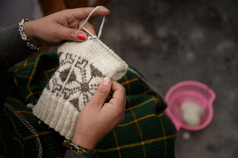 hands of artisan woman knitting star snowflake pattern with grey and white pure sheep wool