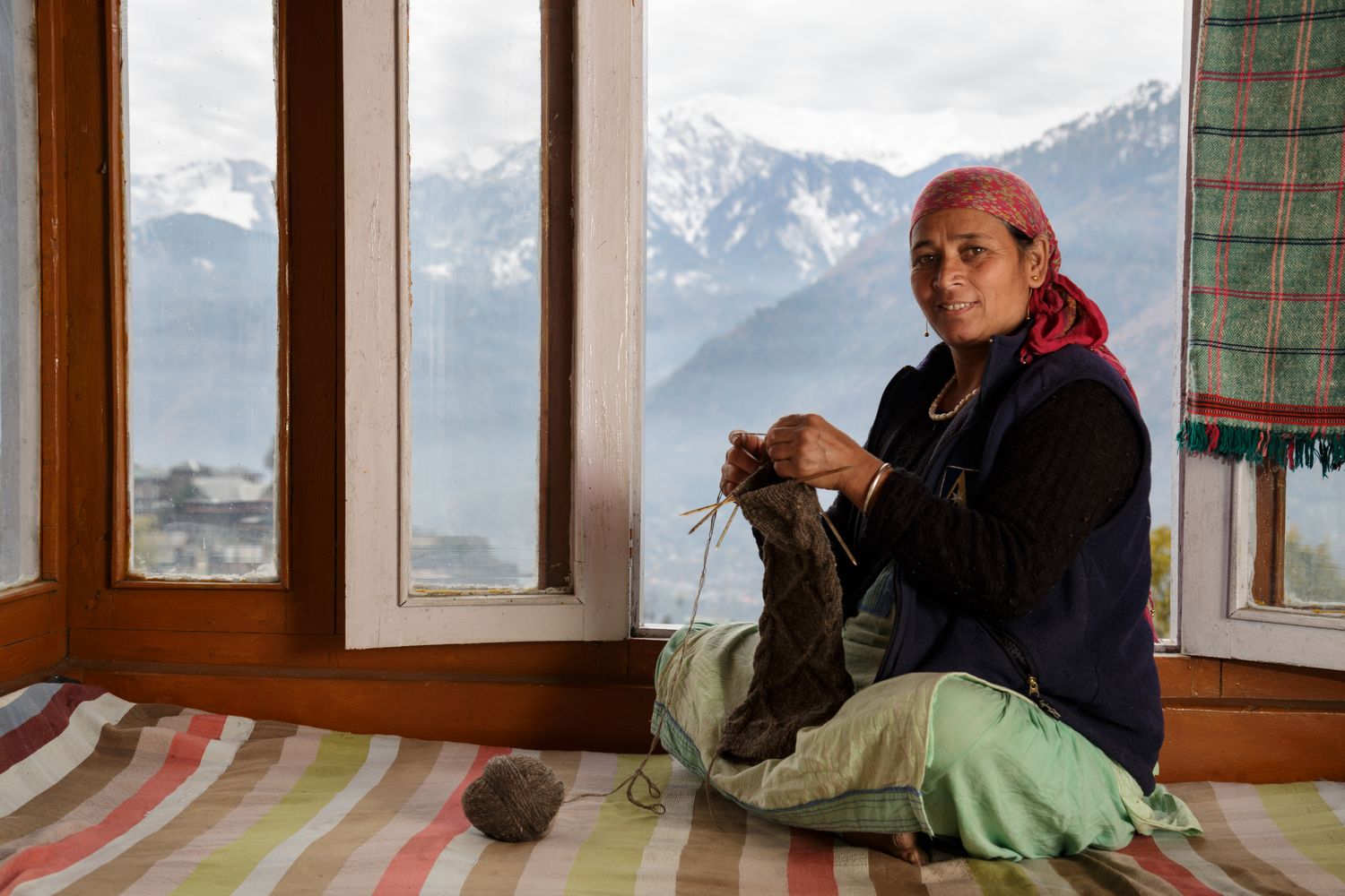 an artisan woman in India holds her grey wool knitting in front of mountain vista