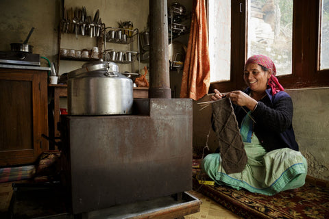 woman artisan gazes smiling as she holds up a grey wool legwarmer she knitted