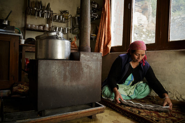 artisan woman in India measures a grey wool legwarmer she knit in her kitchen