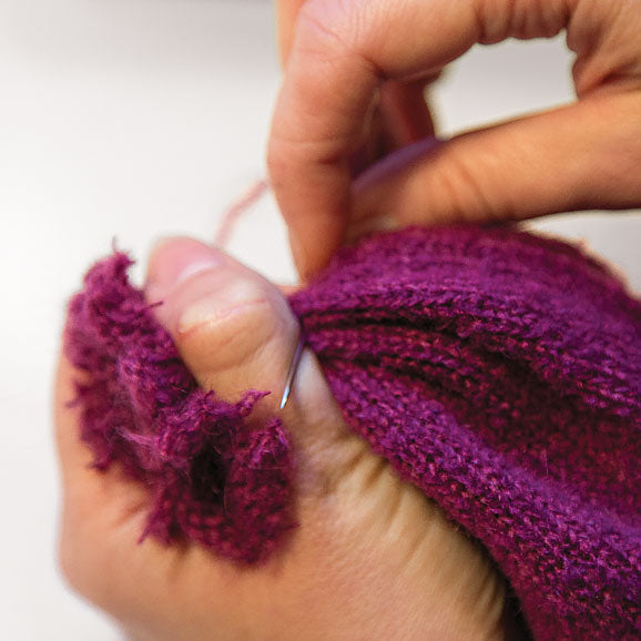 Hand sewing the top of a winter hat.