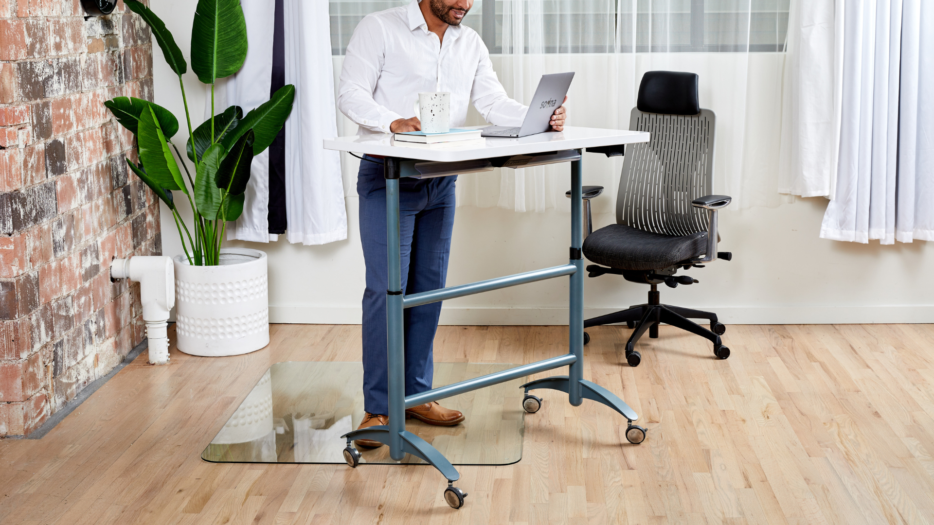 photo of a man in a white shirt standing on a glass chair mat in front of an adjustable height desk