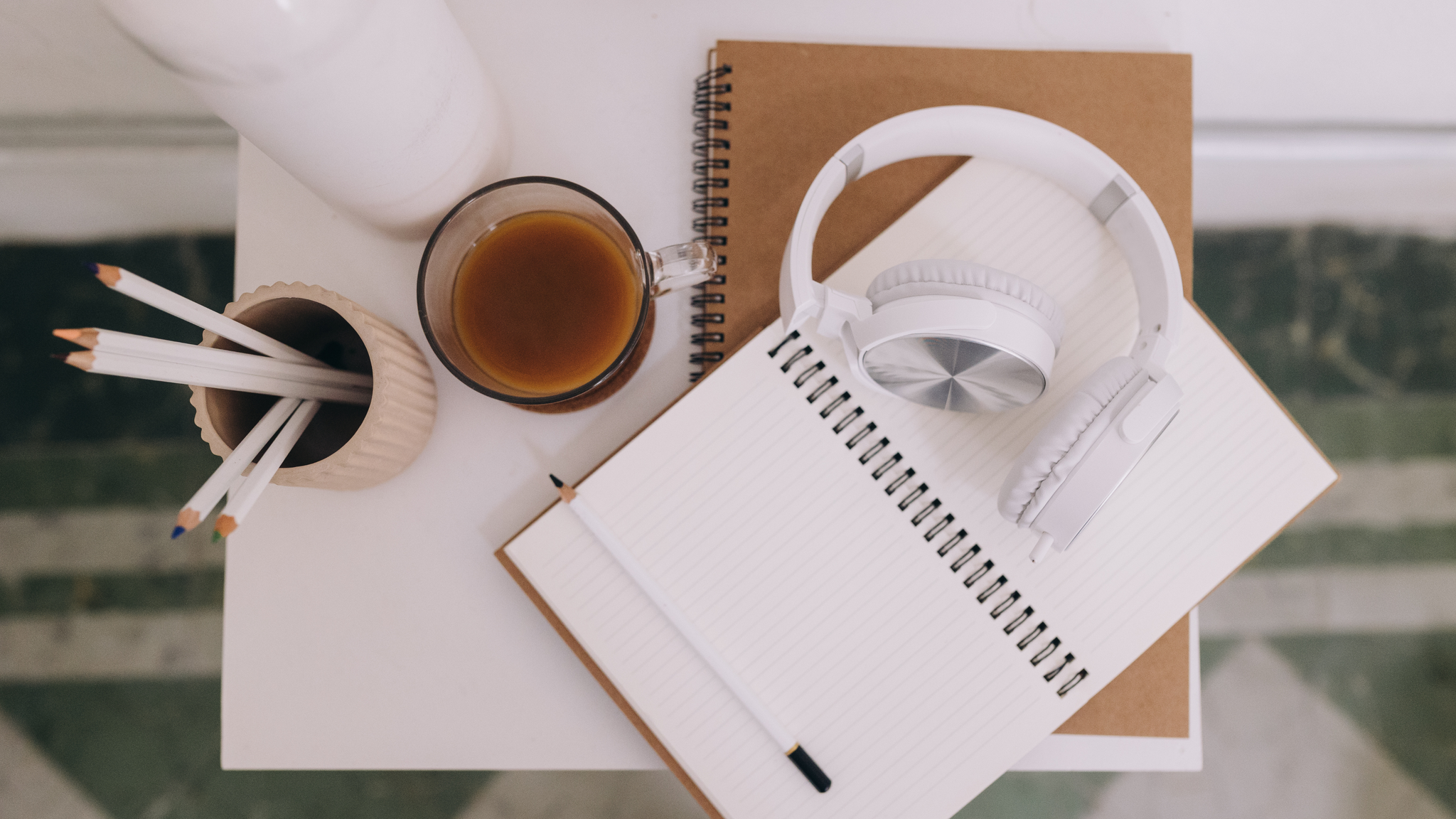 Top down view of an open notebook, headphones, a pencil cup and a coffee cup