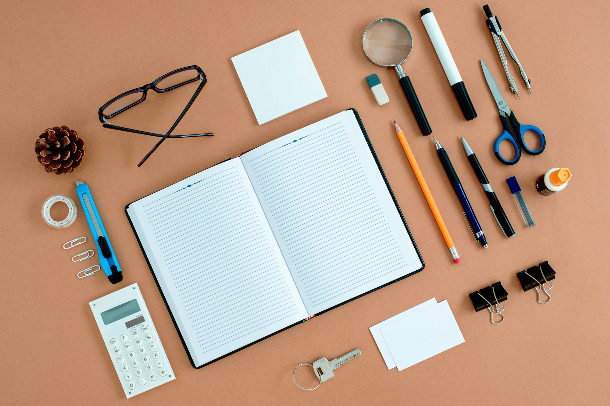 a flatlay image of items you would have in a office such as a notebook, pens, and glasses
