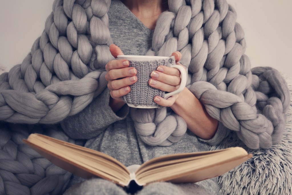 photo of a woman in a chunky knit blanket holding a coffee mug