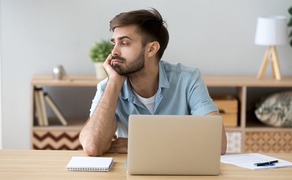 photo of a distracted young man at a table with a laptop