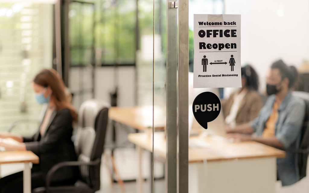 photo of glass office door with sign that reads "welcome back, office reopen, please practice social distancing"