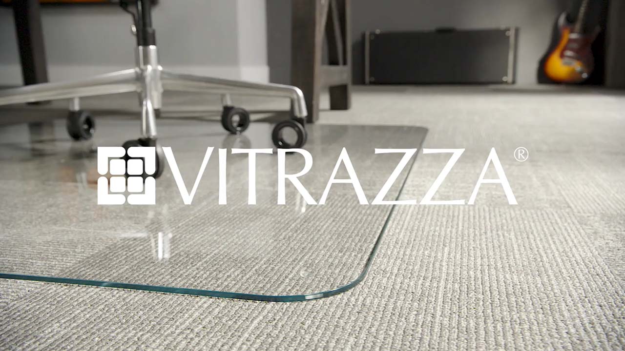 Vitrazza Logo over a photo of a Glass Chair Mat on gray carpet with a guitar in the background