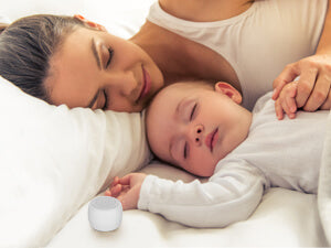 A restful individual asleep, the Babelio Mini Sound Machine visible on the bedside table emitting a soft light and tranquil sounds.