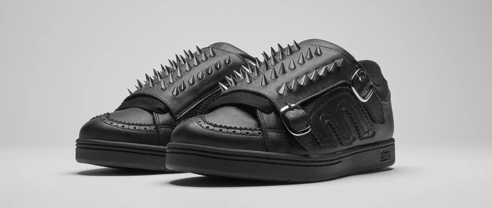 A pair of white sneakers with silver spikes on a black background and a reflective surface.